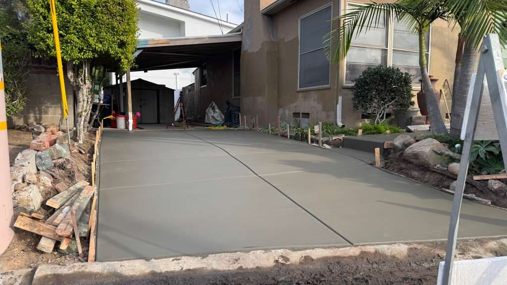 Crew pouring a fresh concrete driveway lined with palm trees on pour day